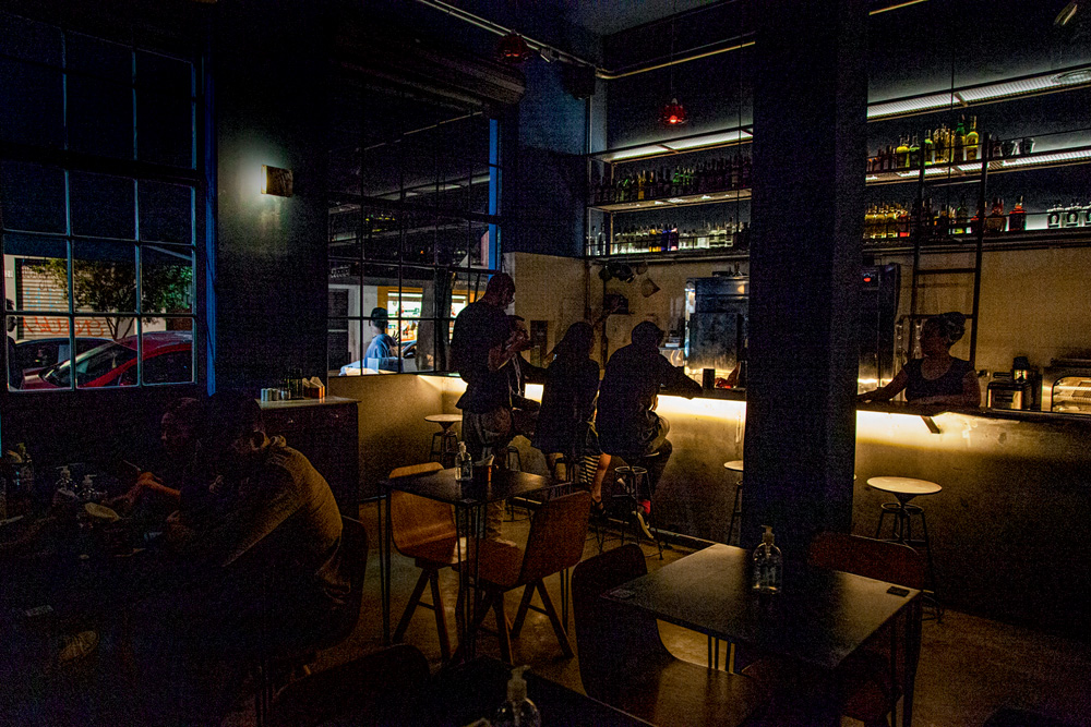 Salão em luz baixa do bar Terê, com balcão ao fundo e mesas.