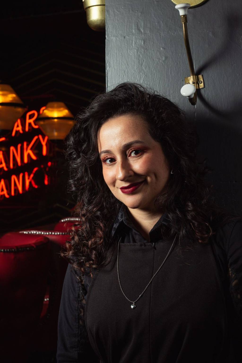 Mulher branca de cabelo preto encostada em parede de bar.