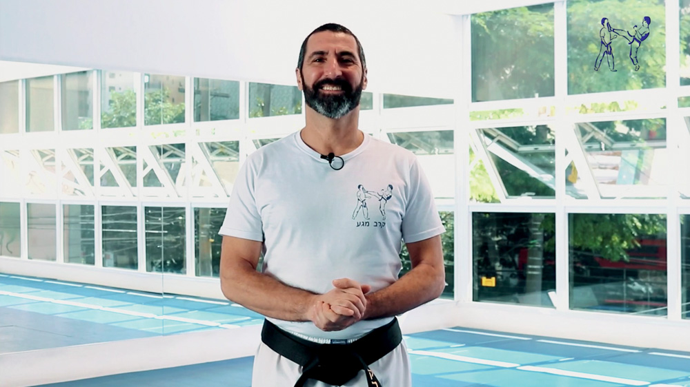 Homem branco de barba posa com camiseta branca, as mãos unidas.