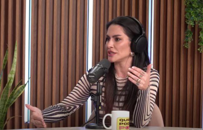 Cleo a imagem mostra cleo, uma mulher branca de cabelos escuros e longos, sentada em um estúdio diante de um microfone