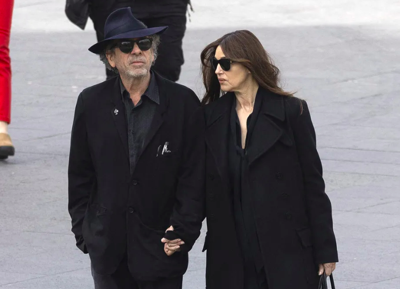 Tim Burton e Monica Belluci de roupas escuras andando de mãos dadas na rua