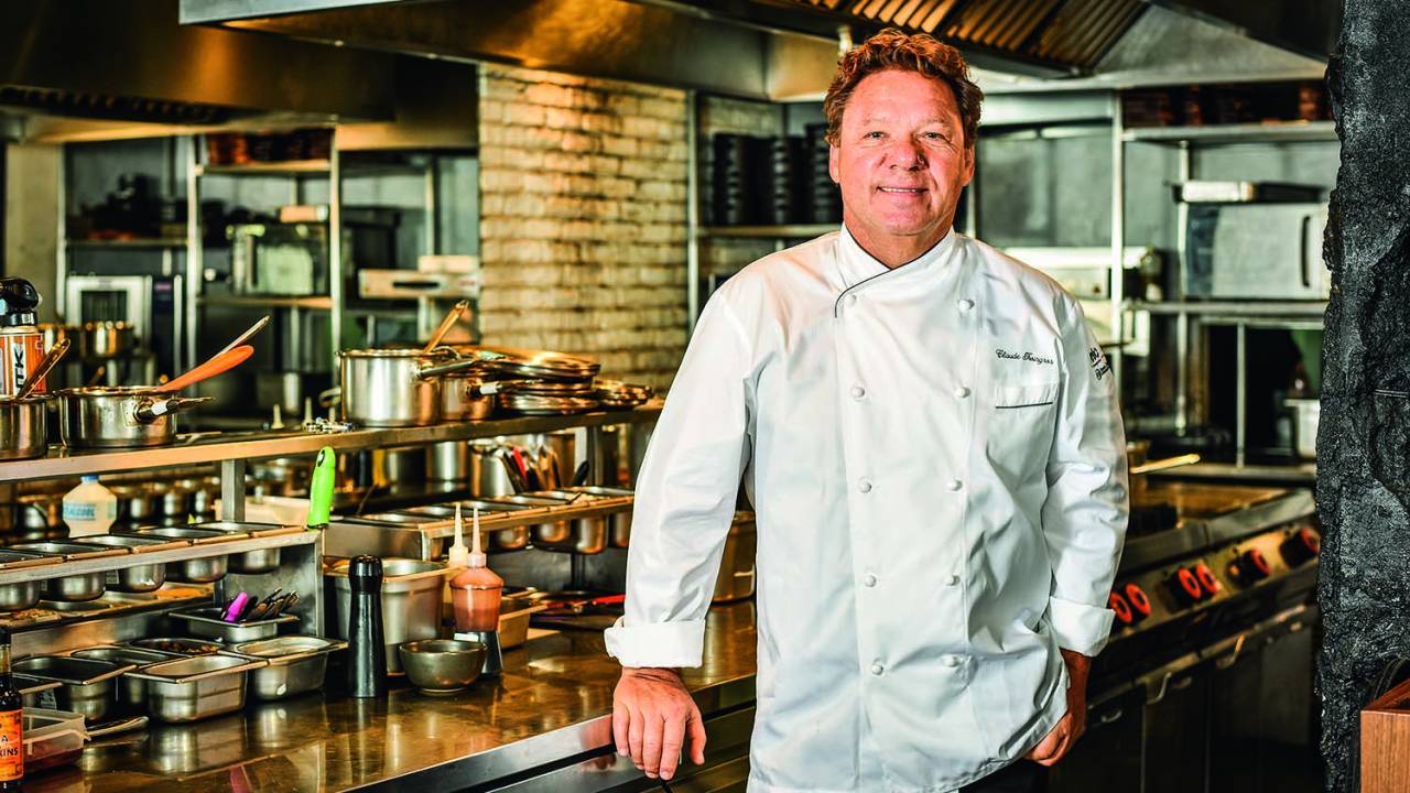 Chef de dólmã apoiado em bancada de cozinha de restaurante.