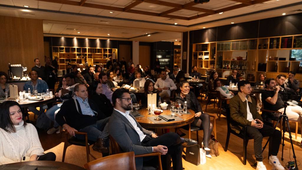 Plateia sentada em restaurante com mesas de madeira e poltronas de couro.