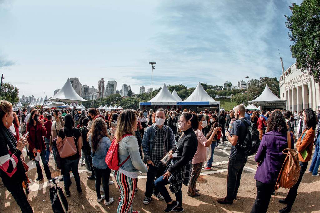 Imagem exibe multidão em área aberta com tendas ao fundo.