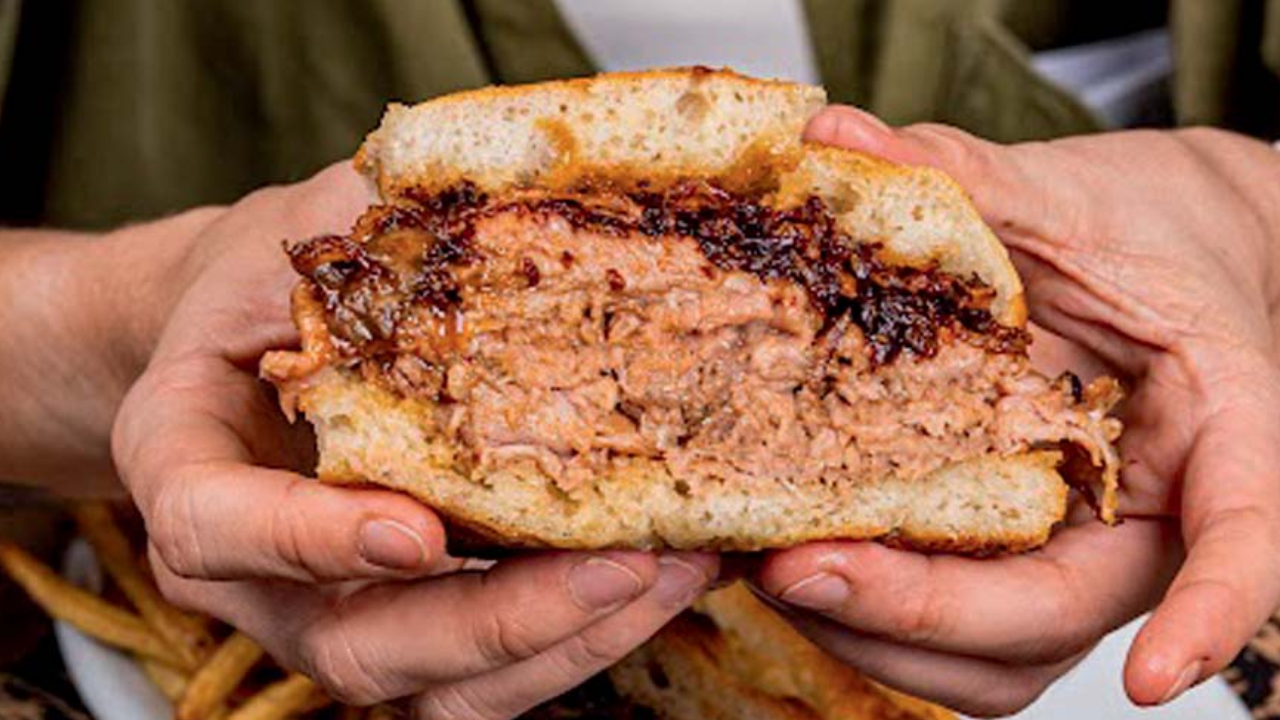Mãos segurando sanduíche bem recheado de carne com molho.