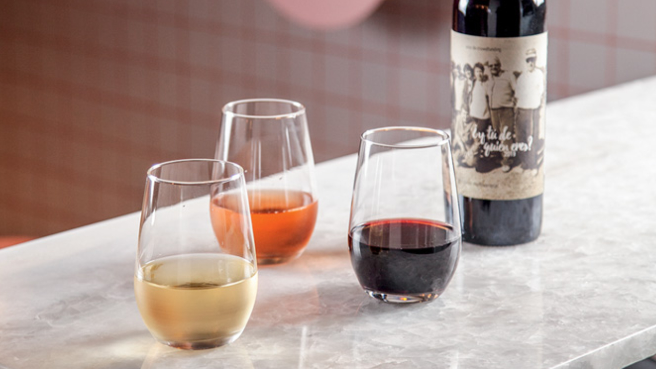 Balcão de mármore com três taças de vinhos, um rosé, um branco e um tinto e uma garrafa ao fundo.