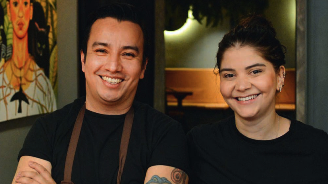 Casal de chefs lado a lado sorrindo para a foto.