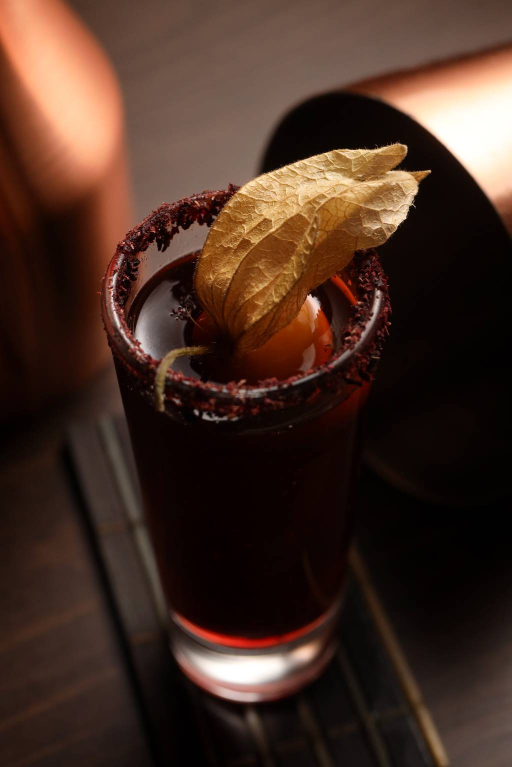 Drink roxo em copo alto com borda com crosta roxa e fisális por cima.