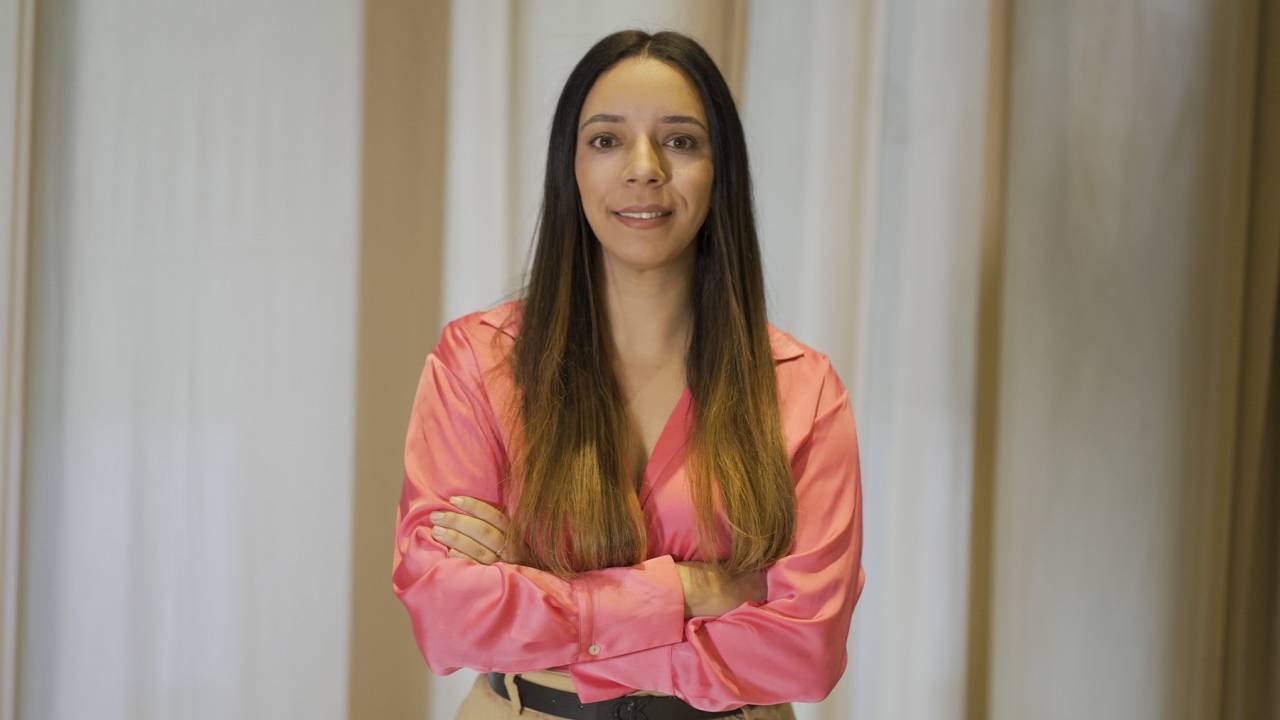 Mulher de cabelos lisos posa de braços cruzados com camisa rosa.