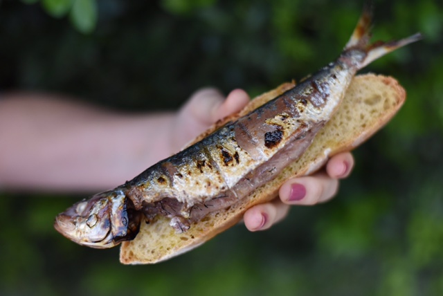 Mão segurando pão com sardinha inteira assada.