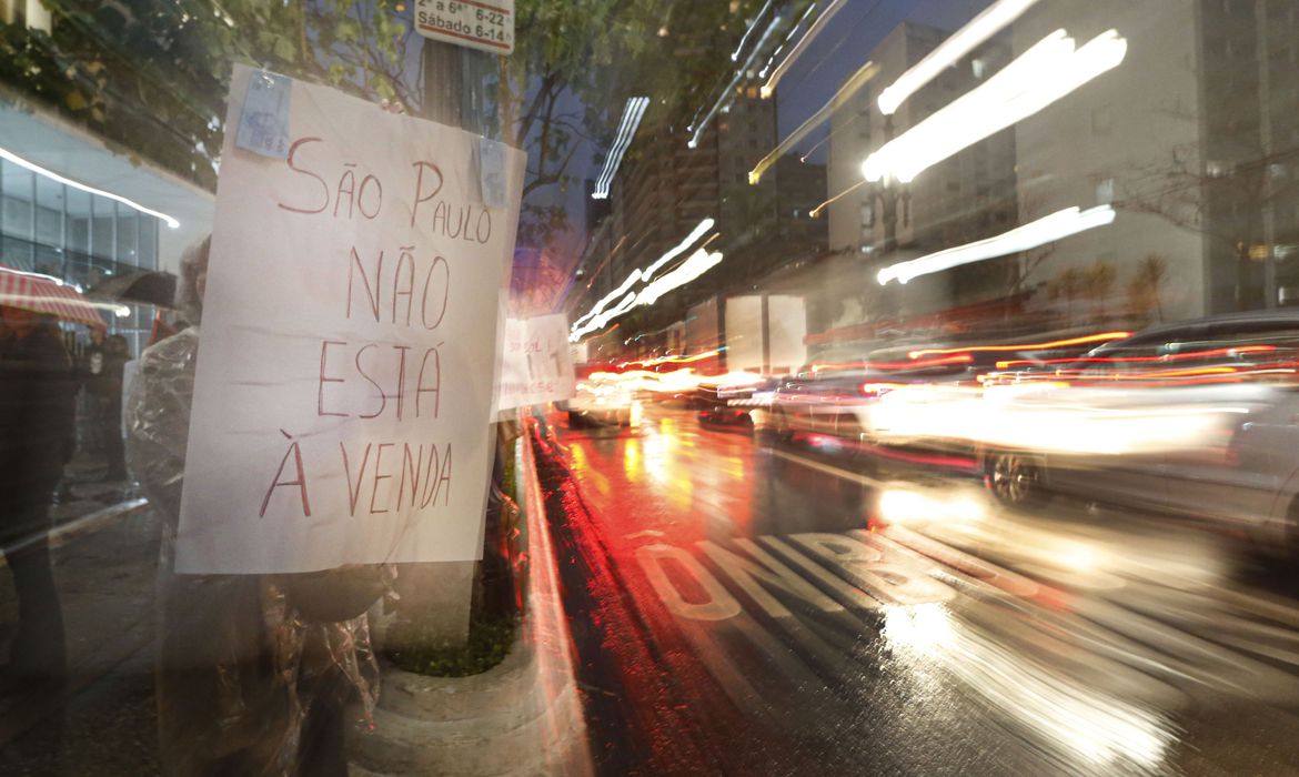 a imagem mostra uma pessoa na calçada segurando um cartaz com os dizeres "são paulo não está à venda"