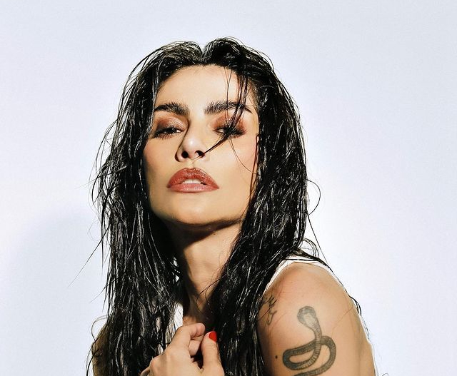 a imagem mostra cleo pires, uma mulher branca, com tatuagens nos braços, de cabelos longos e escuros molhados olhando para a câmera
