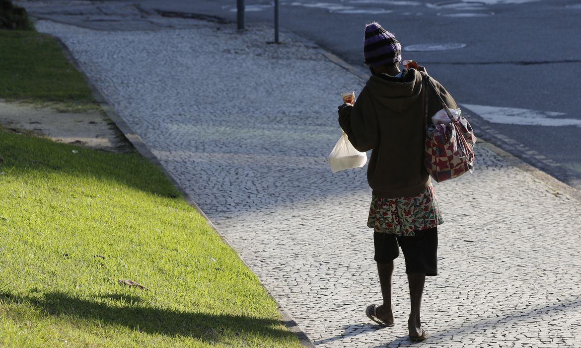 uma pessoa em situação de rua caminhando caminhando, vista de costas