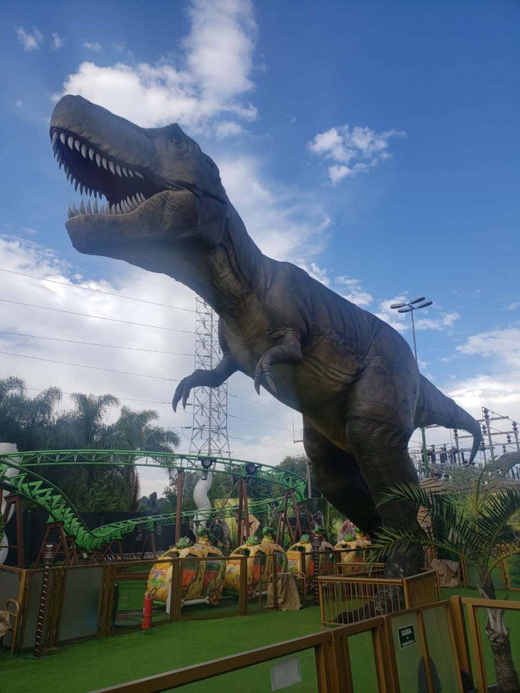 Maquete de tiranossauro rex ao lado de montanha-russa.