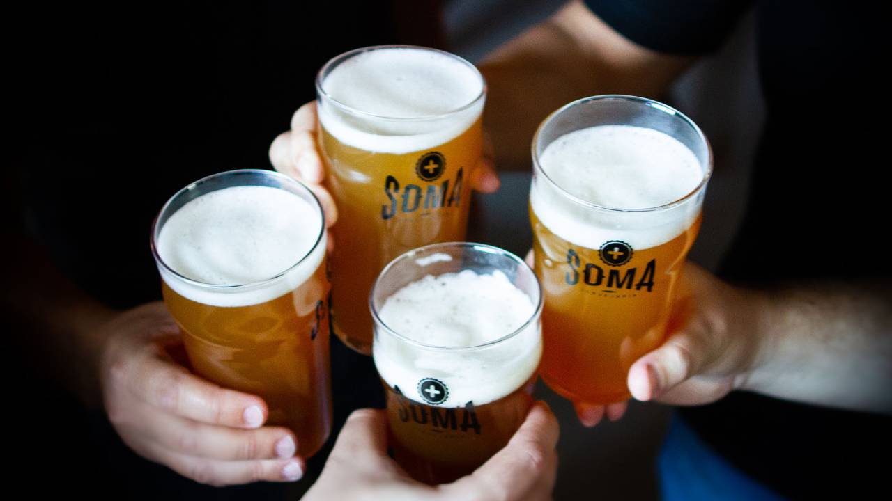 Quatro mãos segurando copos de vidro com cerveja brindam.