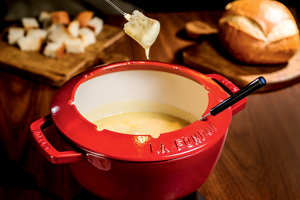 Panela vermelha de fondue de queijo sobre mesa de madeira.