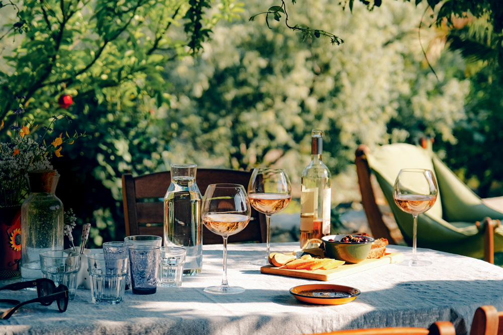 Mesa de piquenique ao ar livre no meio de árvores com taças de vinhos.