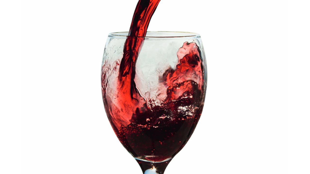 Zoom em taça de vinho sendo servido com vinho tinto no fundo branco.