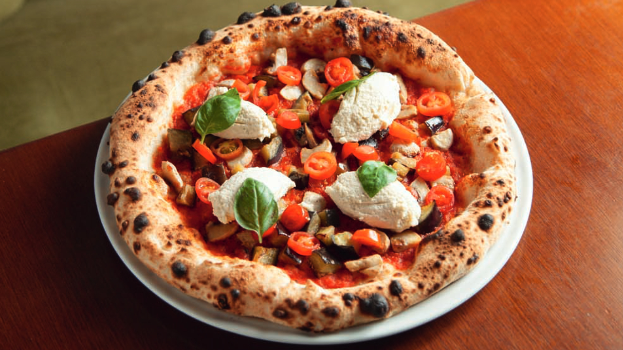 Pizza individual sobre mesa de madeira com tomates.