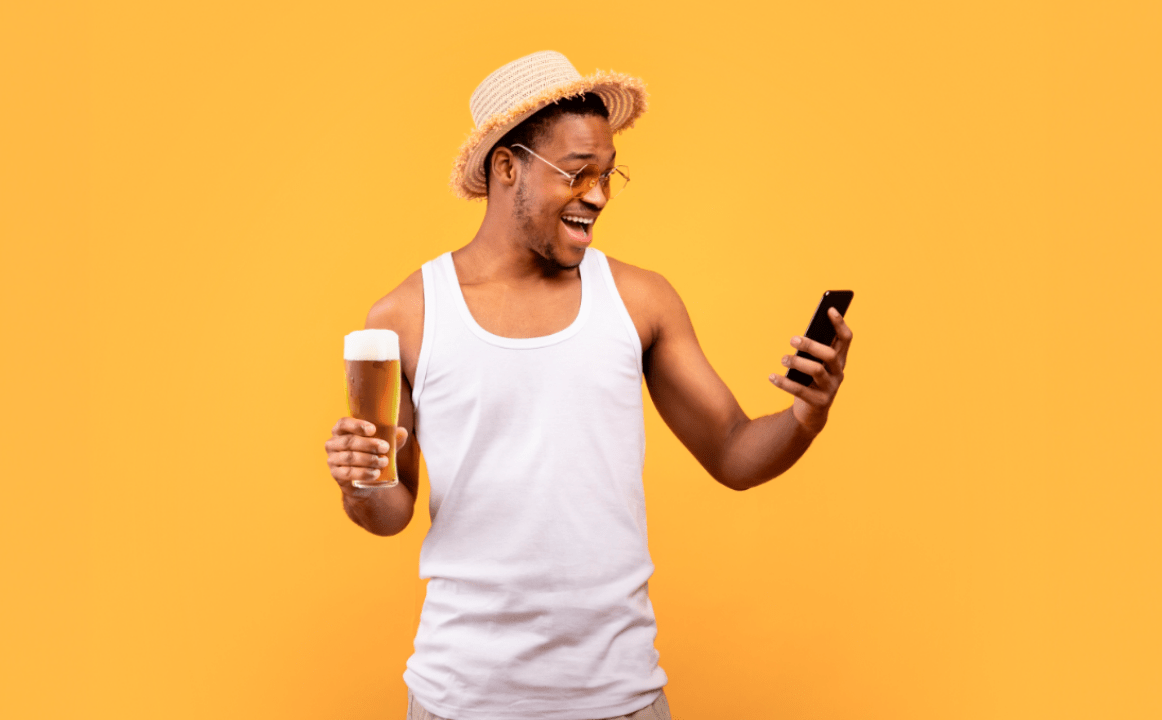 Homem segurando um copo de cerveja em uma mão e um celular na outra