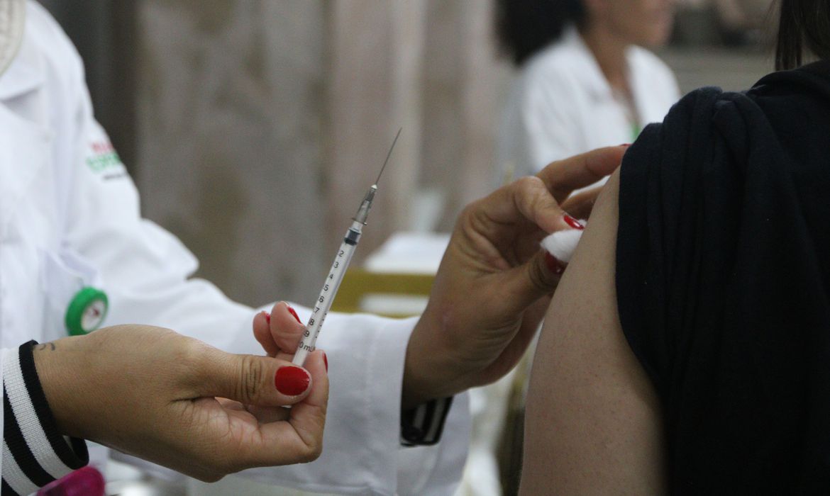 a imagem mostra uma enfermeira com uma seringa e o braço de uma pessoa que será vacinada