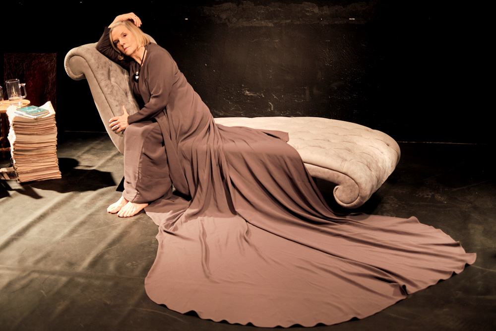 a atriz em cima de um divã com um longo vestido que se espalha pelo divã e pelo chão