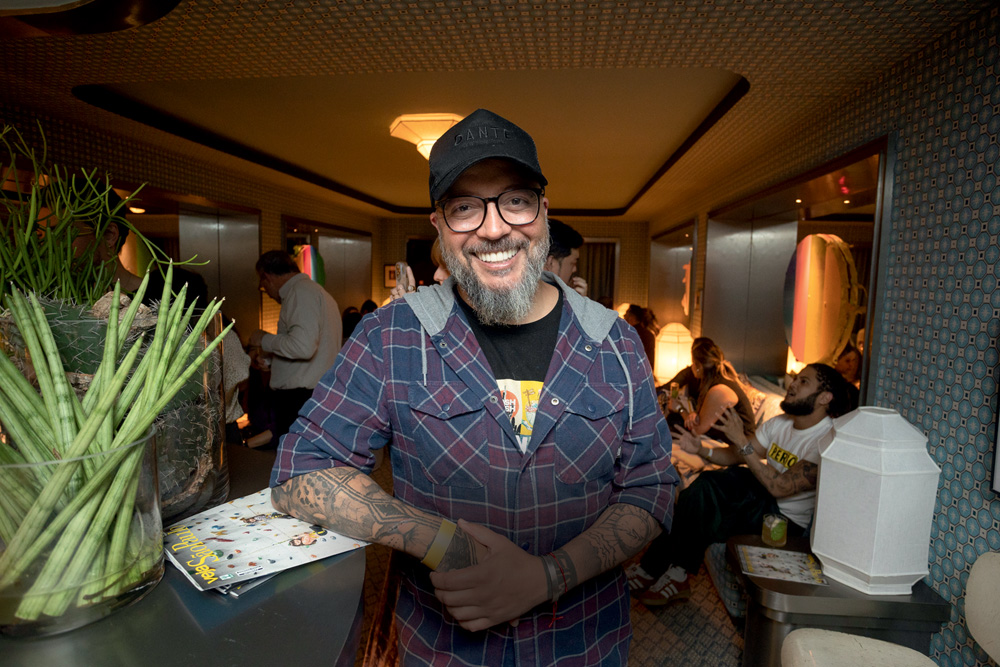 Homem de barba grisalha e boné preto com braço encostado em balcão de bar olhando para a foto.