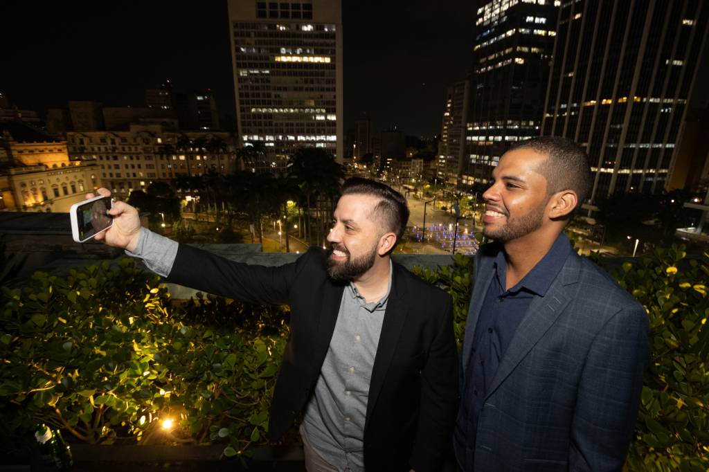 Imagem mostra dois homens tirando selfie em cenário urbano