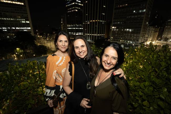 Imagem mostra três mulheres sorrindo em foto com vista para o centro de São Paulo