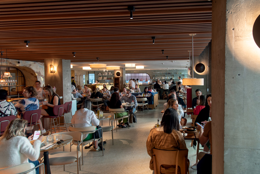 Salão do restaurante A Casa de Antônia, com teto de madeira e mesas ocupadas por pessoas.