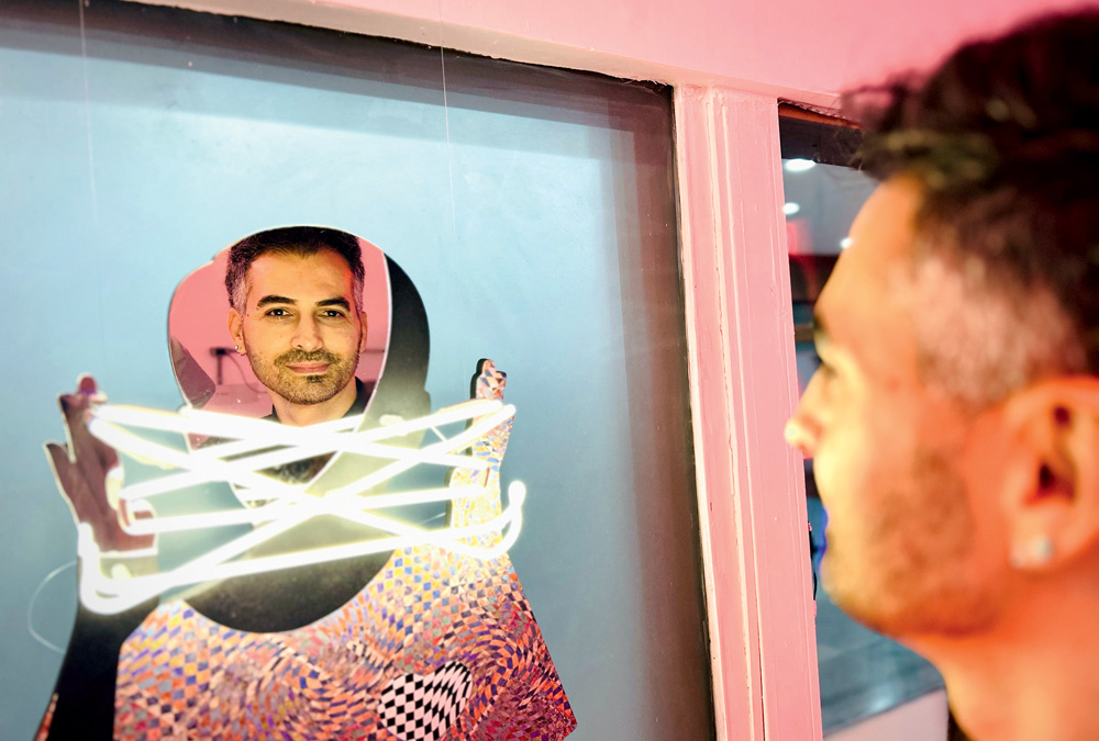 Homem branco de barba encara um espelho adornado por neons.