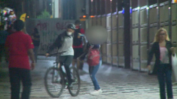 homem em cima de uma bicicleta roubando uma mulher na rua, à noite