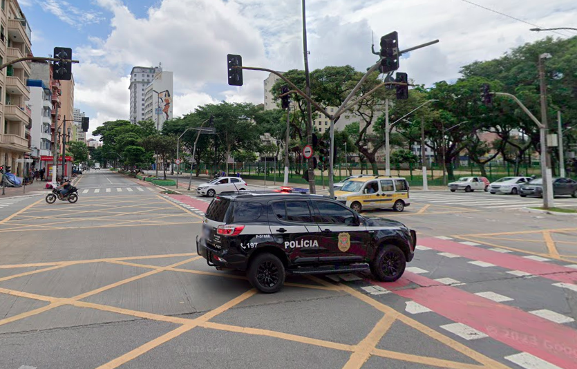 uma viatura da polícia civil passando pelo cruzamento de uma grande avenida