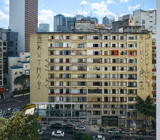 Imagem mostra Edifício Virgínia, com cerca de 10 andares em rua com leve subida em região com muitos prédios