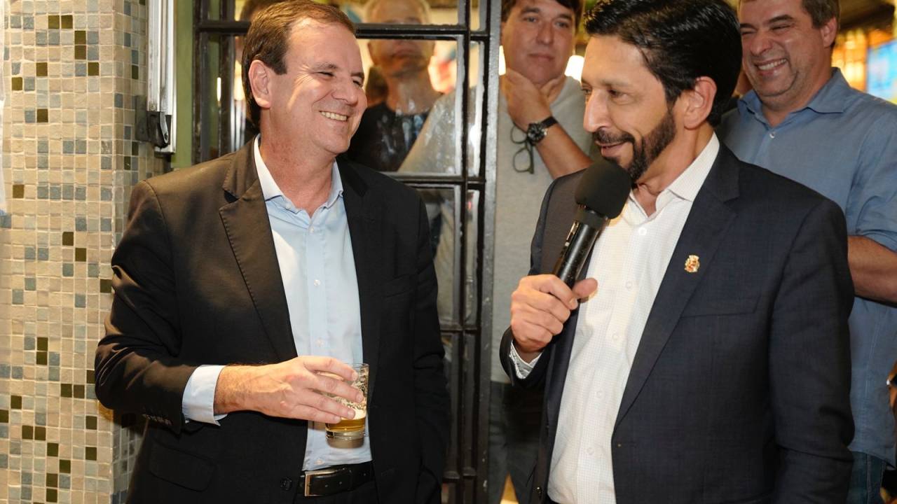 A imagem mostra Eduardo Paes e Ricardo Nunes lado a lado sorrindo.