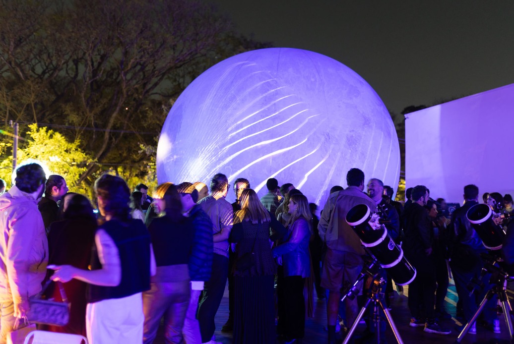 Foto exibe multidão ao redor de uma esfera iluminada que imita uma lua.
