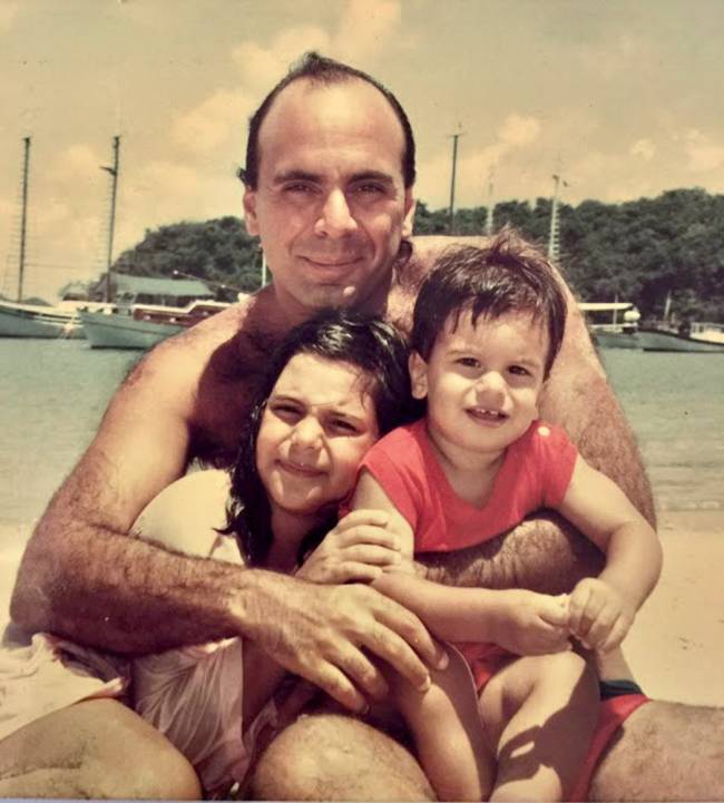 Foto antiga mostra Arnaldo abraçando os dois filhos, ainda crianças, em praia