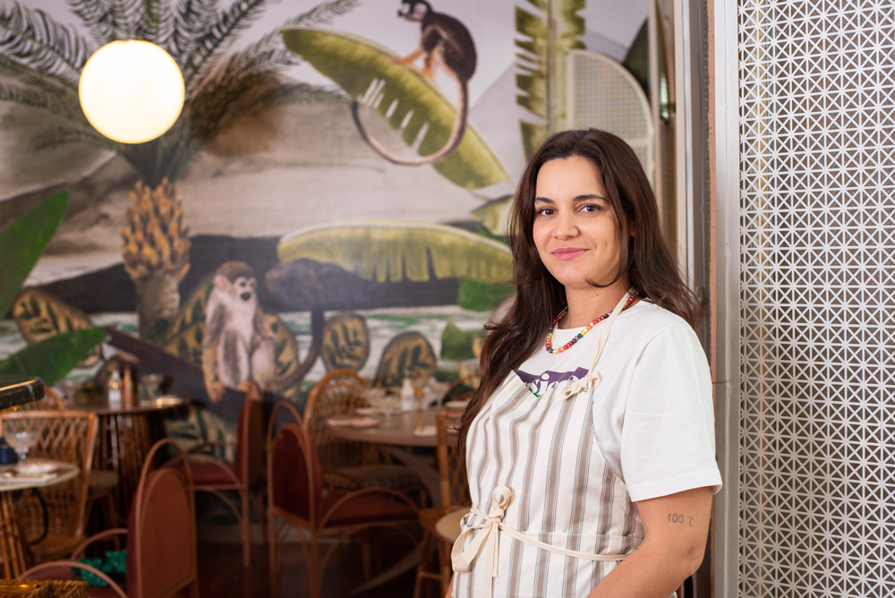 A chef Renata Vanzetto encostada na parede do restaurante Mico grávida vestindo avental.