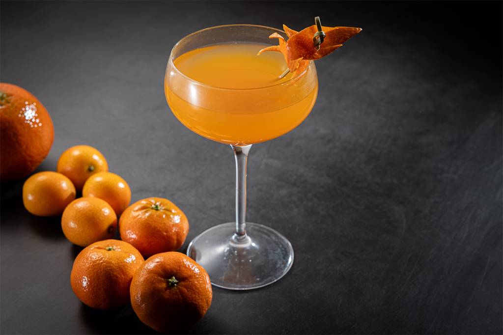 Japan House AizomÊ Taça com drinque laranja ao lado de mini tangerinas.