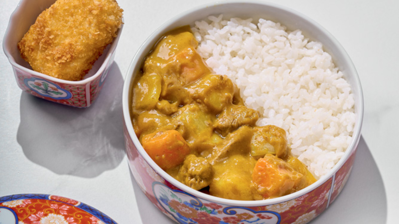 Tigela de louça com arroz e curry sobre tampo branco.