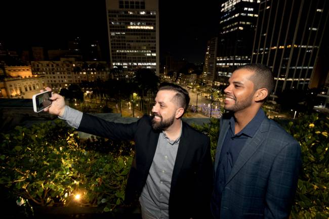 Imagem mostra dois homens fazendo selfie em terraço