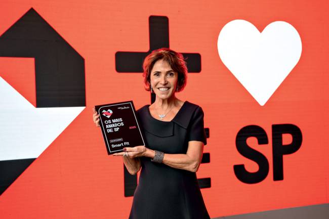 Imagem mostra mulher segurando placa da Smart Fit no prêmio