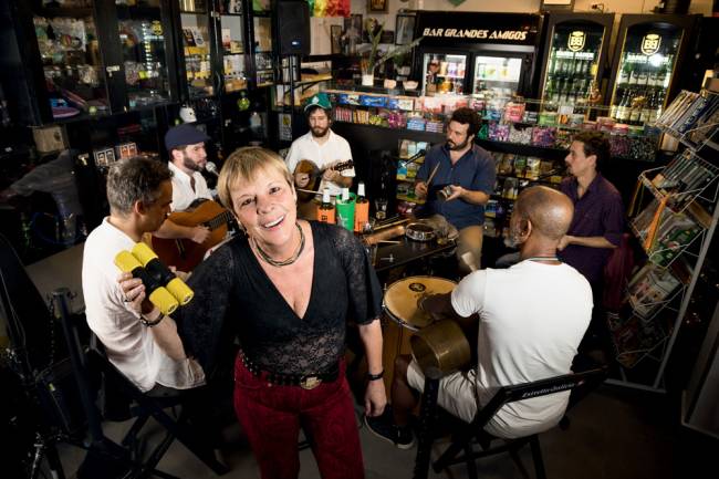 Imagem mostra Vânia em primeiro plano e, ao fundo, roda de samba em interior de bar