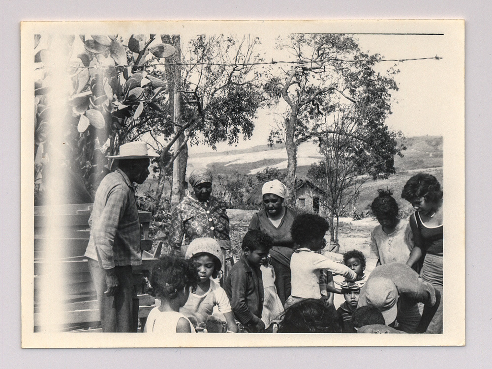 Foto em preto e branco exibe grupo de pessoas em zona rural.