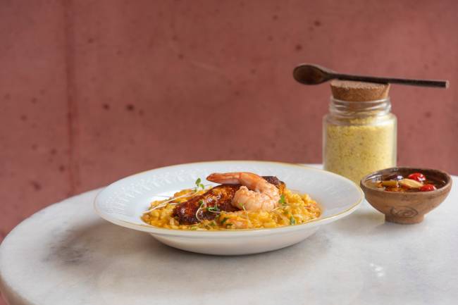 Prato de louça branca com arroz coberto por camarão em mesa de tampo branco.