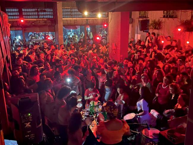 Imagem mostra, em canto direito, roda de samba e, ao fundo, grande quantidade de pessoas dentro de bar