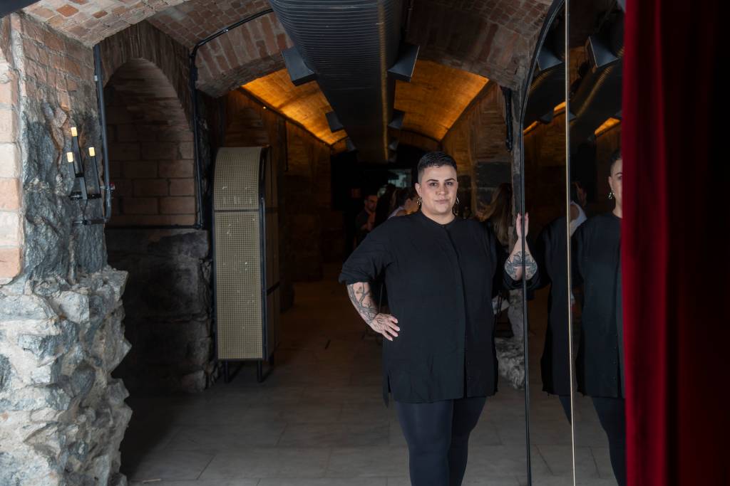 Mulher toda de preto de cabelo curto com a mão direita na cintura.