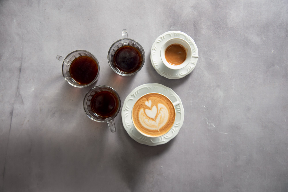 Diversas xícaras de café e cappuccino vistas de cima em fundo cinza.