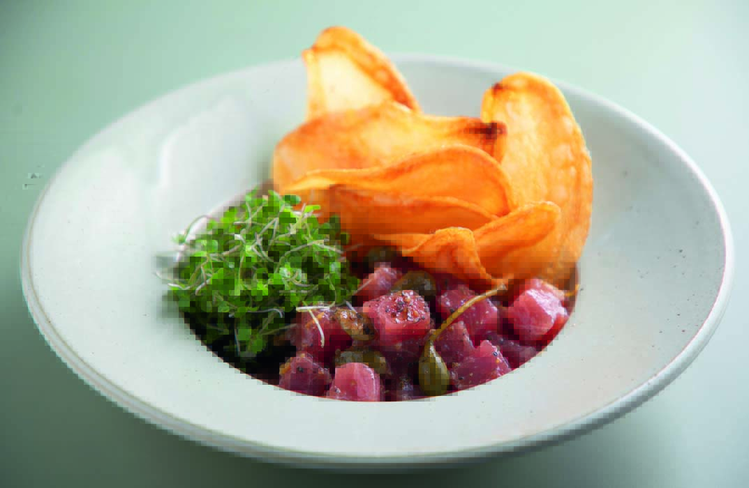 A imagem mostra um prato fundo branco visto de cima com algumas folhas verdes, pedaços de batata bem finos e atum picado.