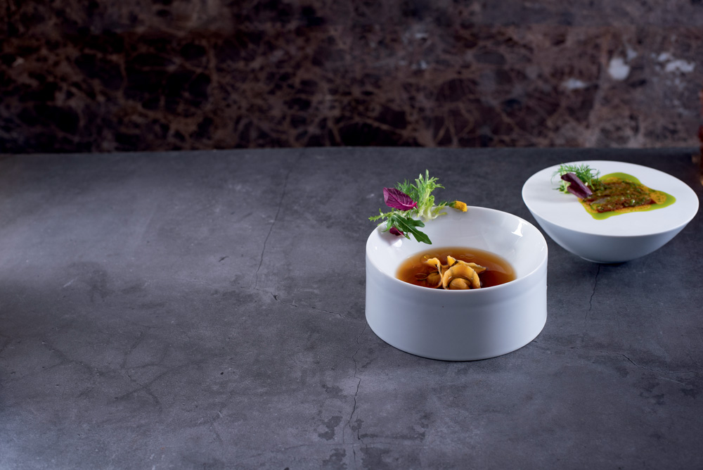 Um prato fundo branco com totellini e caldo dentro sobre uma mesa de concreto.